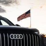 Frontale Audi nera con bandiera americana al tramonto