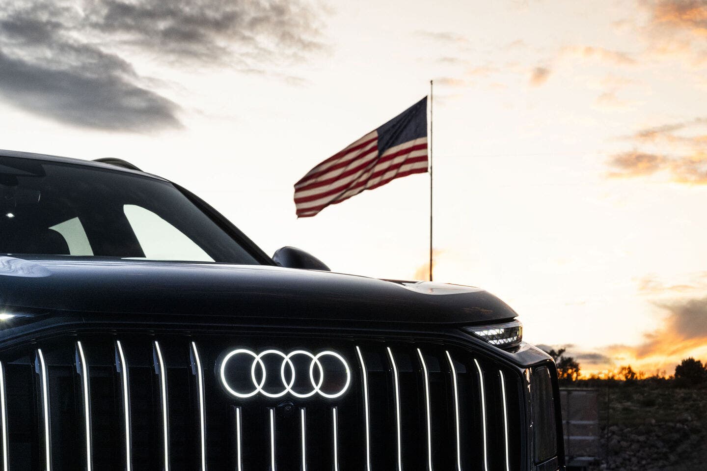 Frontale Audi nera con bandiera americana al tramonto