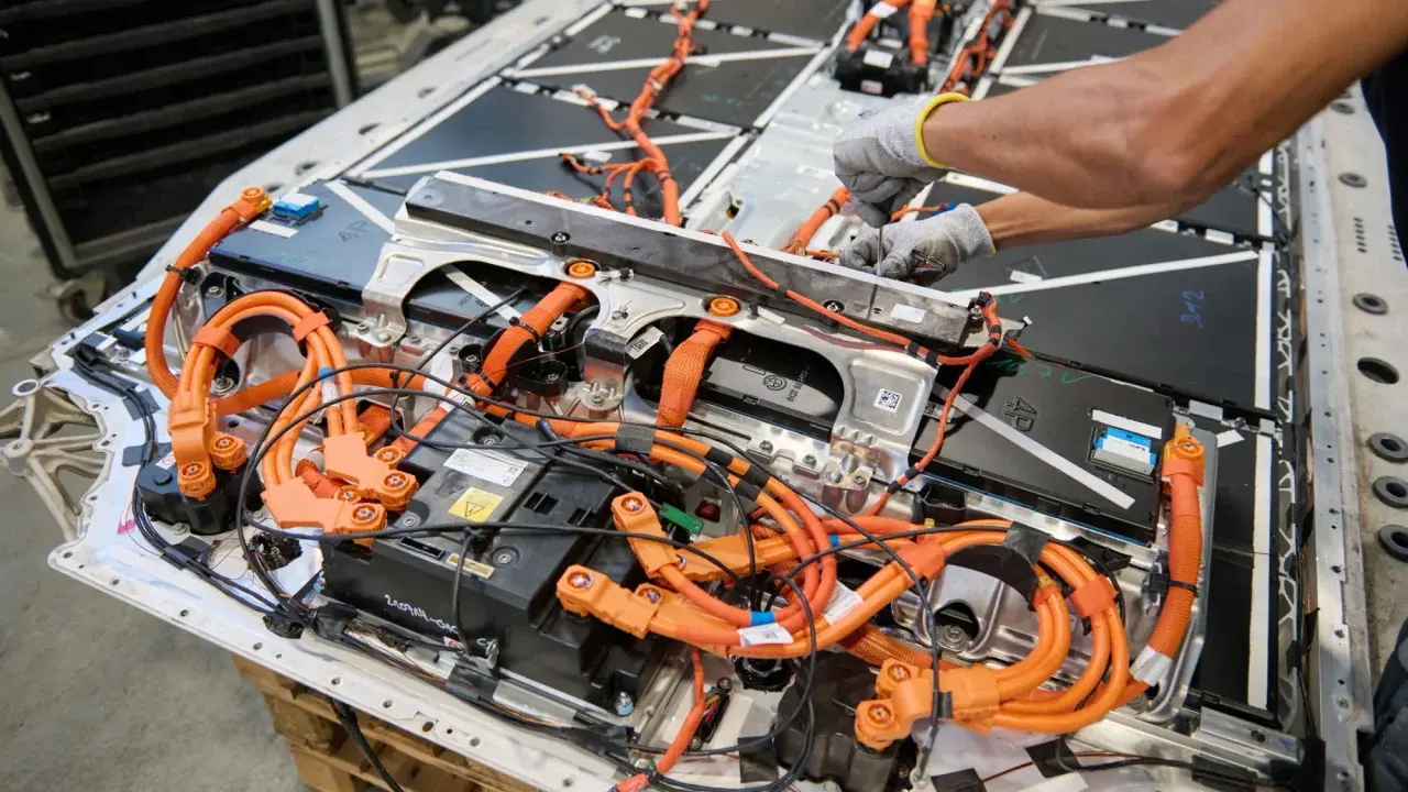 Tecnico assembla cablaggi arancioni su batteria di auto elettrica
