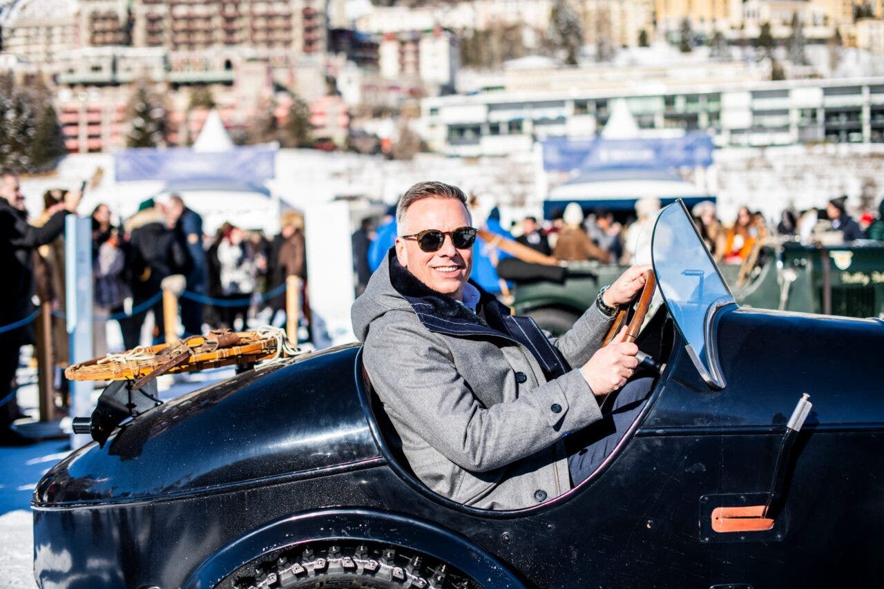 Uomo sorridente guida auto d’epoca durante evento invernale
