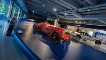 Auto da corsa d’epoca rossa esposta in un museo Maserati, con altre auto sullo sfondo